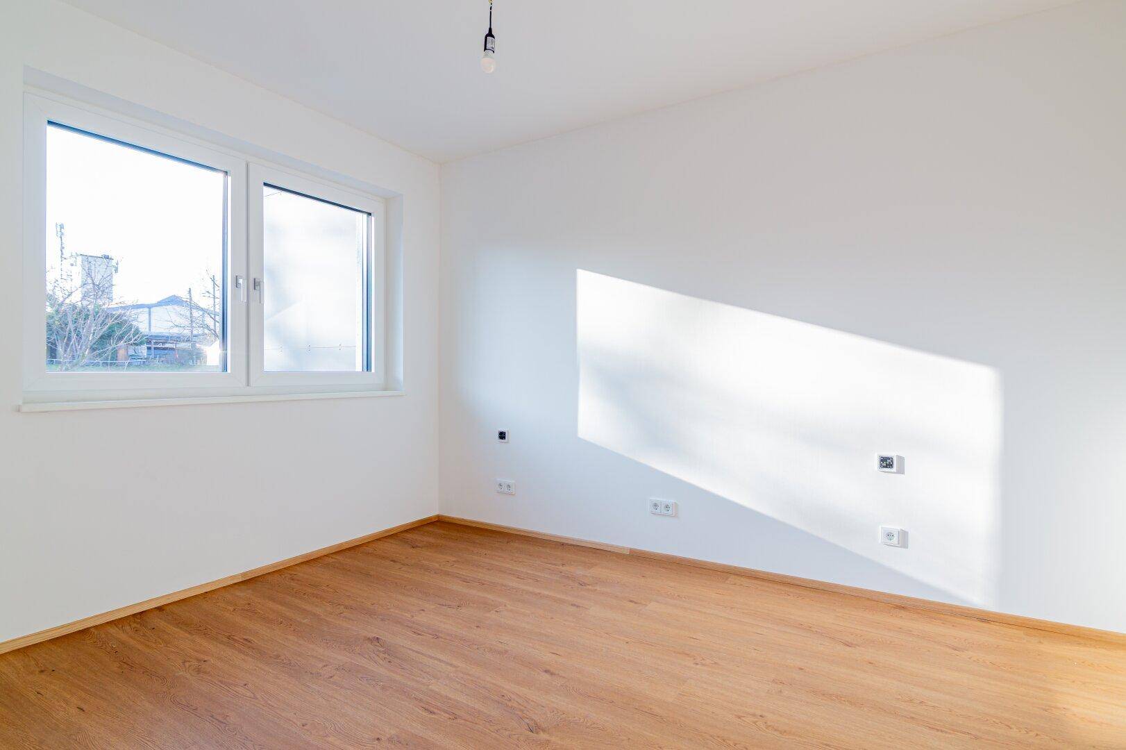 Helles Zimmer mit Holzboden und einem Fenster, das viel Tageslicht hereinlässt, sehr freundlich.