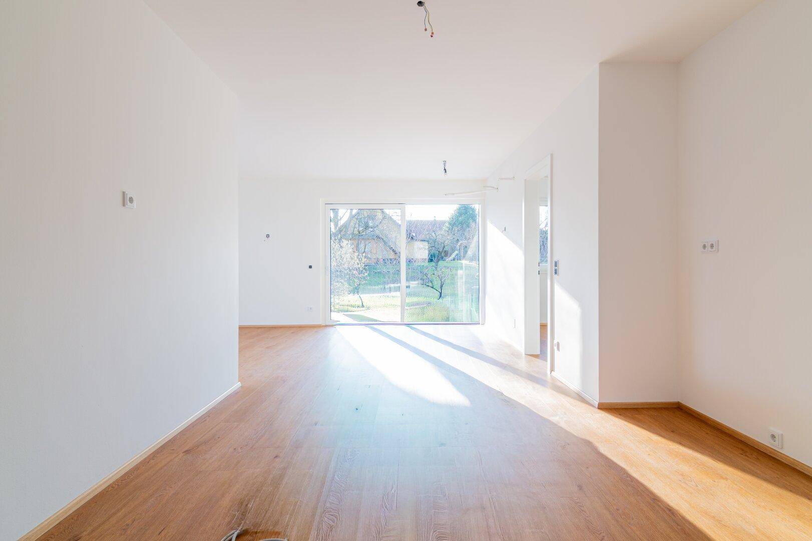 Lichtdurchfluteter Wohnbereich mit Holzboden und großen Fenstern zum Garten, sehr einladend.