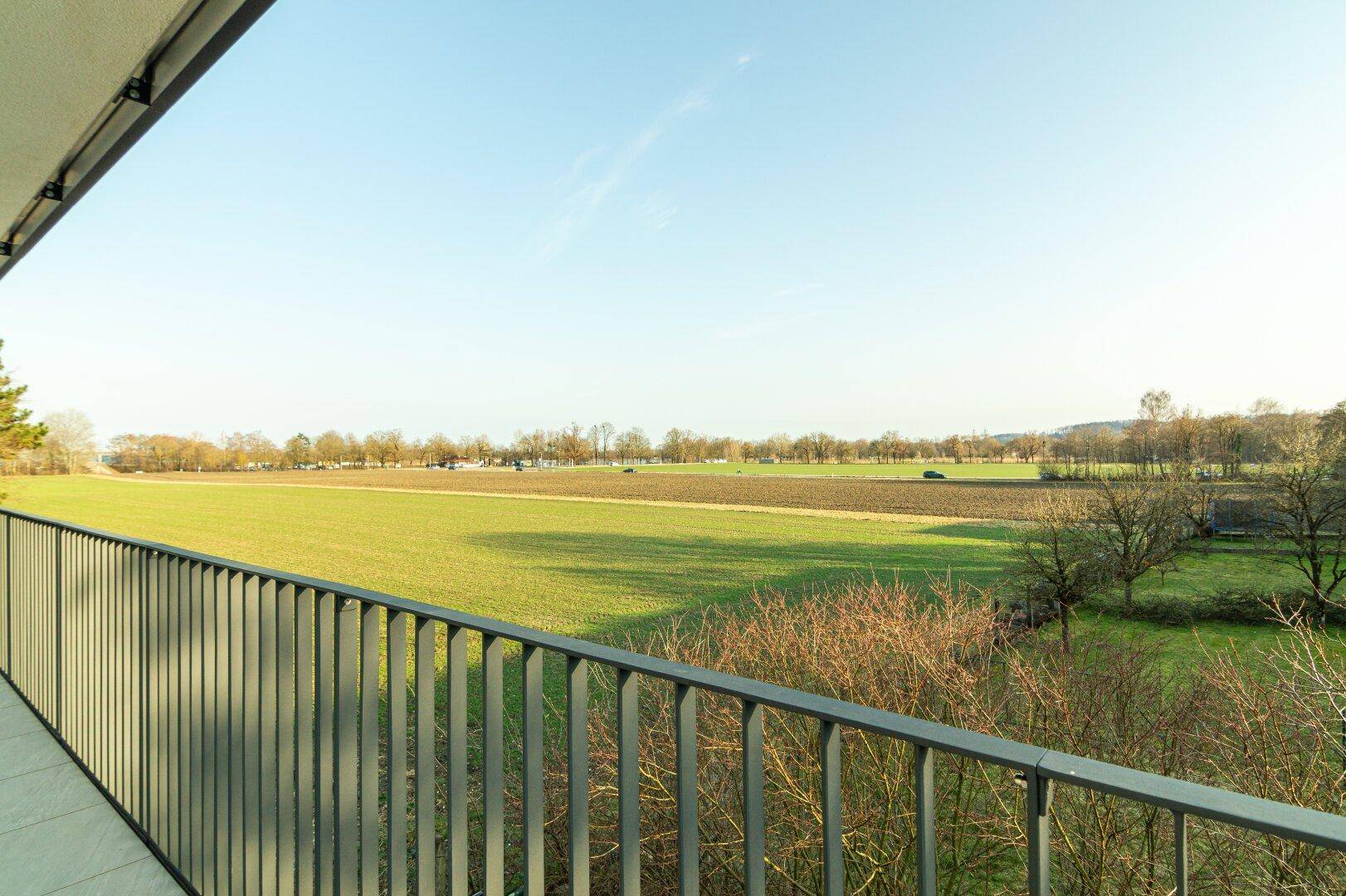 Panoramablick vom Balkon auf weite Felder und den klaren Himmel, der viel Helligkeit verspricht.