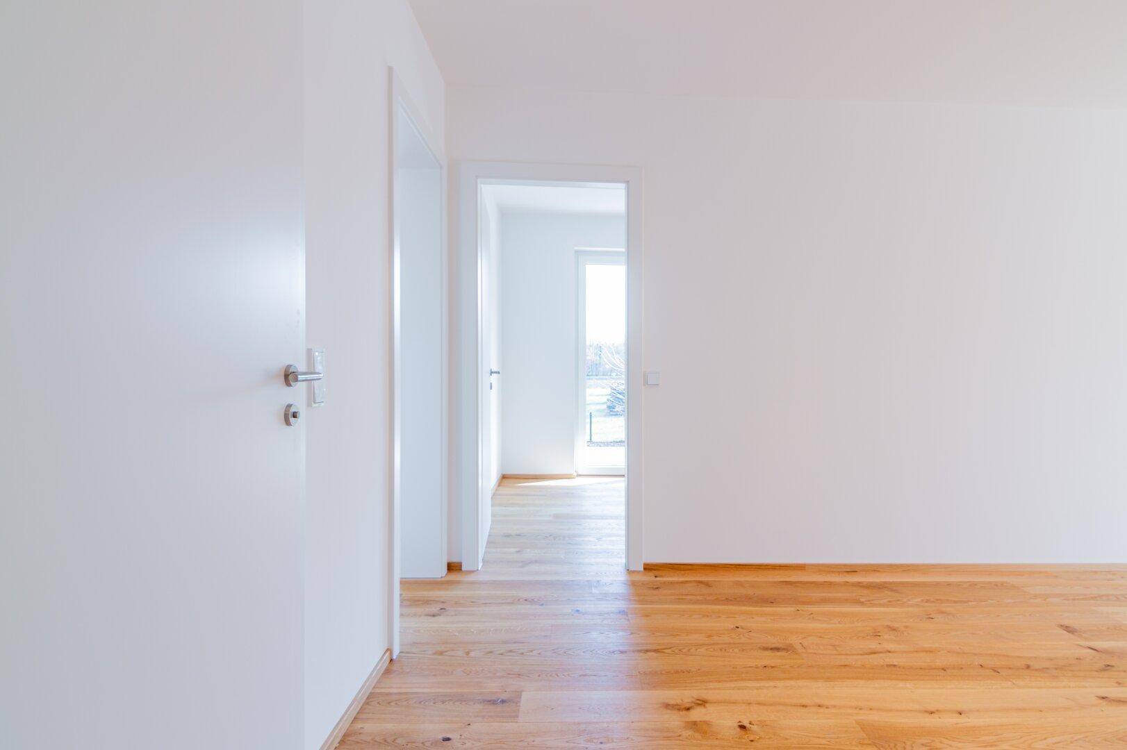Heller Flur mit Holzboden und Zugang zu einem weiteren lichtdurchfluteten Raum.