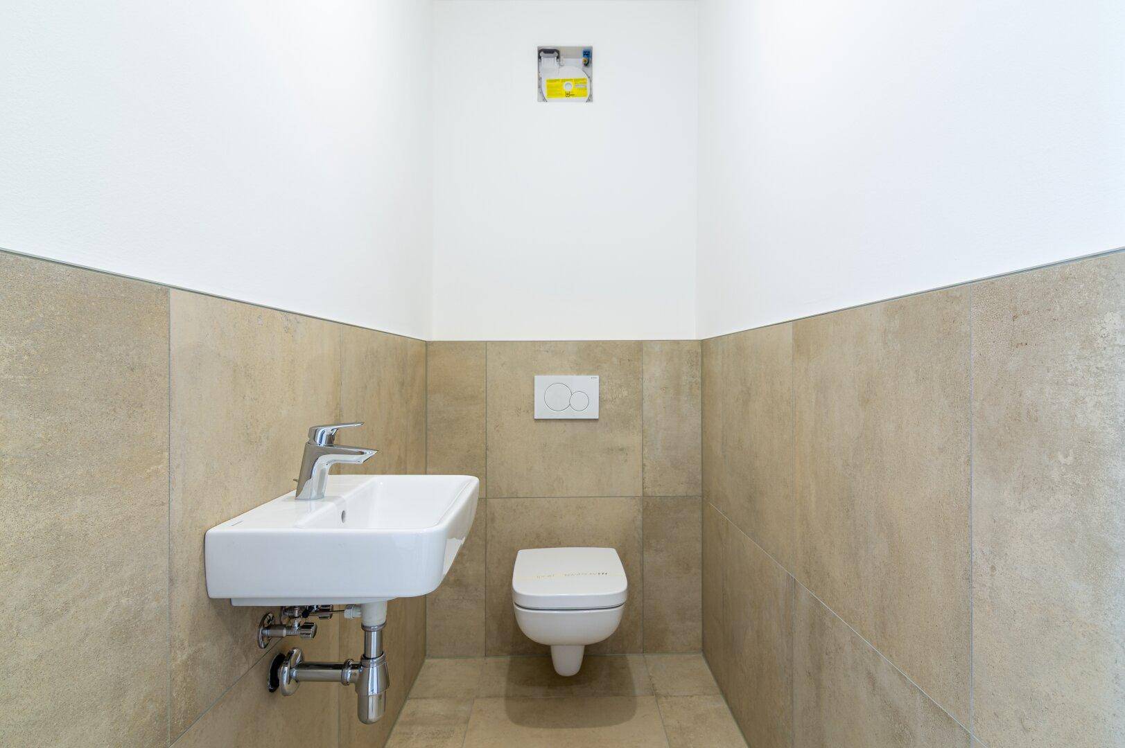 Gäste-WC mit beigefarbenen Fliesen, wandhängendem WC und modernem Waschbecken.