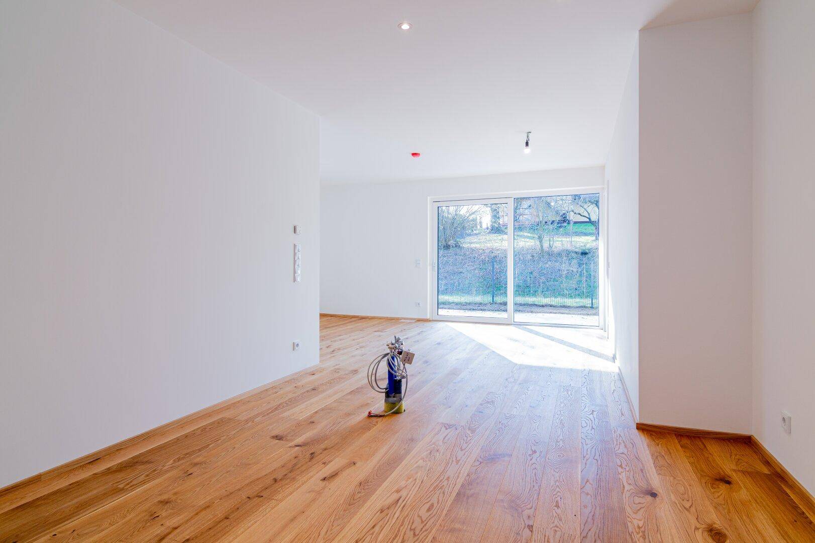 Geräumiger, heller Raum mit Holzboden und großer Schiebetür zum Gartenbereich.