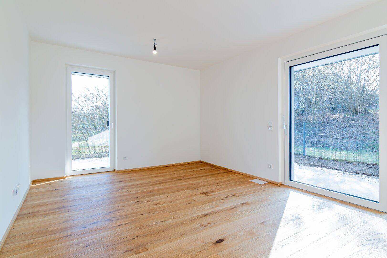 Heller Raum mit Holzboden und großen Fenstern, die viel Tageslicht hereinlassen.