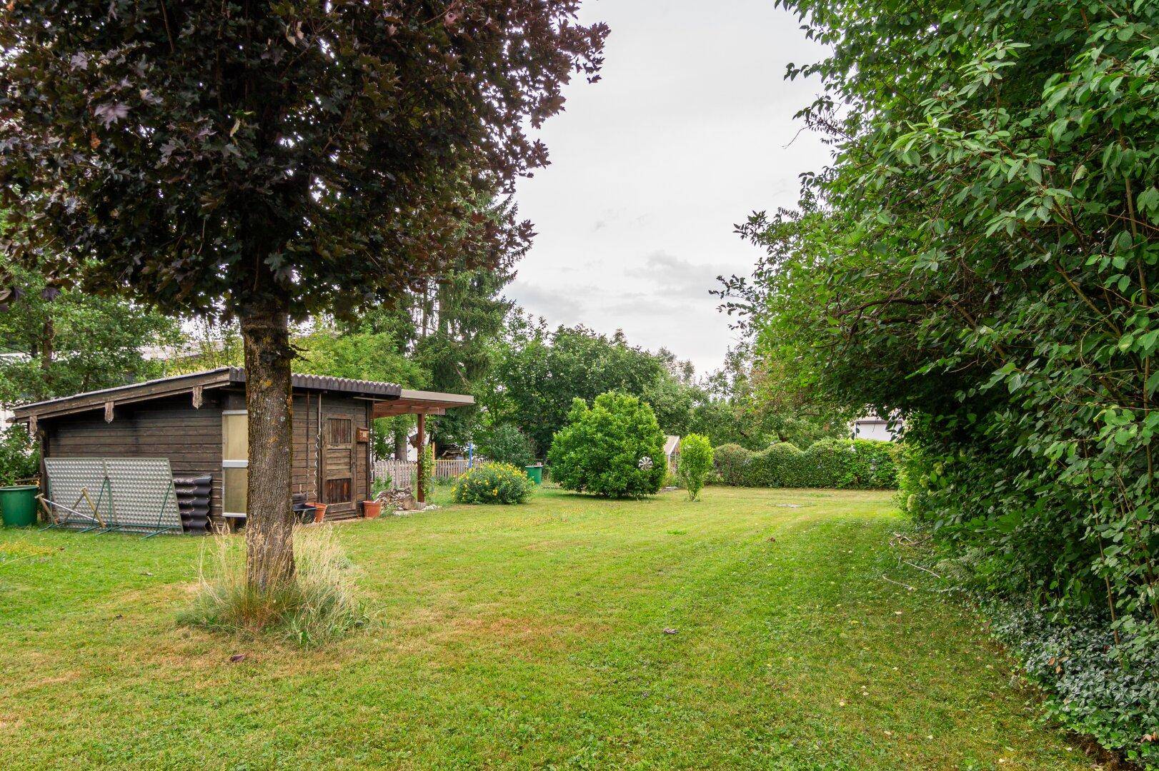Großer Garten mit Rasenfläche, Bäumen und einem kleinen Holzschuppen im Hintergrund.