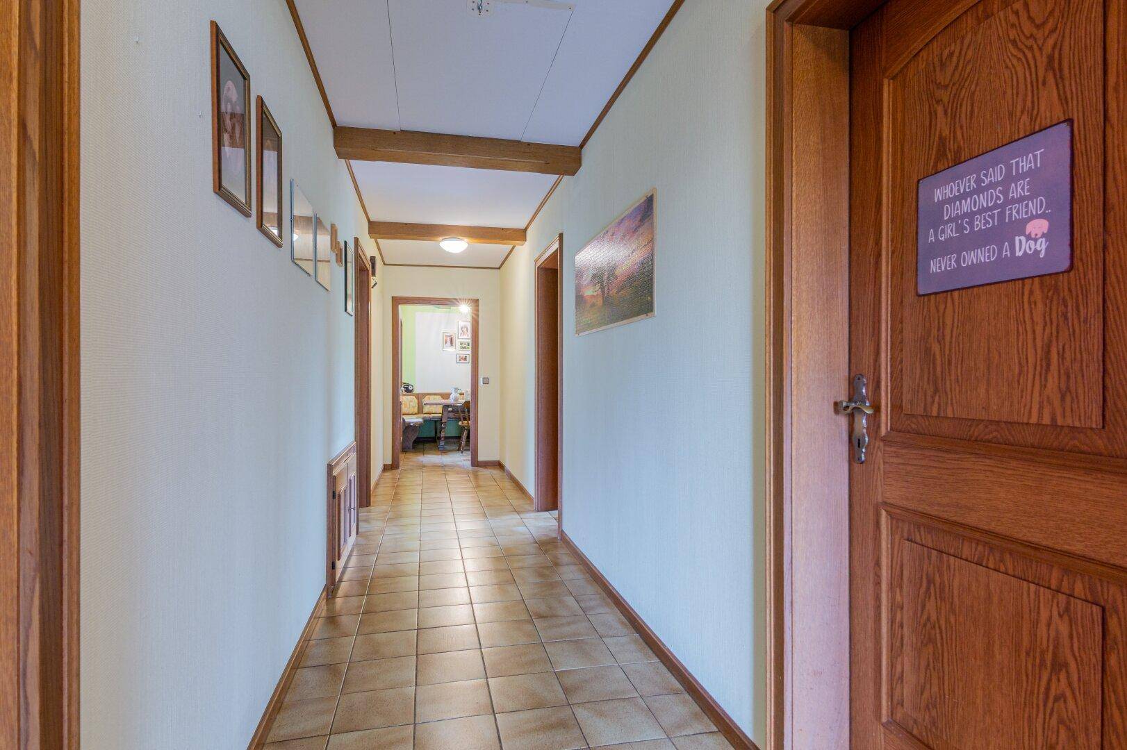 Langer Flur mit Fliesenboden und Holztüren, der zu weiteren Räumen im Haus führt.