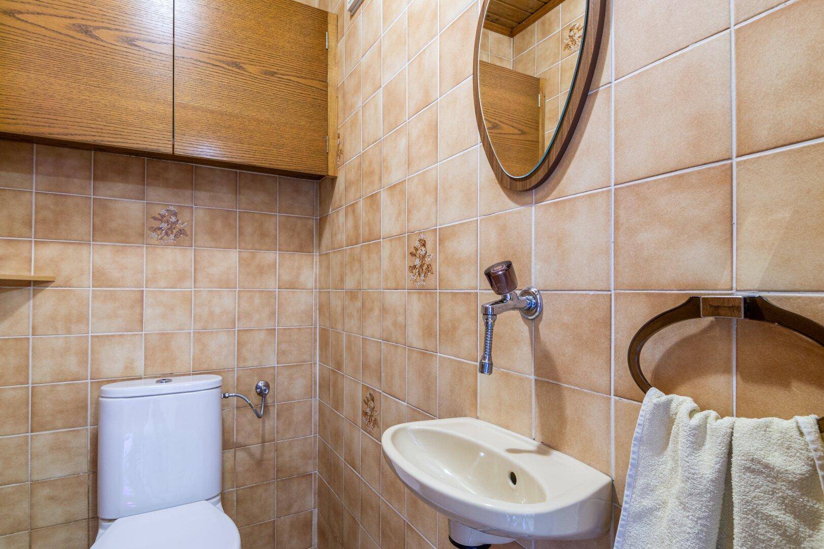 Kleines Gäste-WC mit braunen Fliesen und einem Waschbecken, funktional und einfach gehalten.