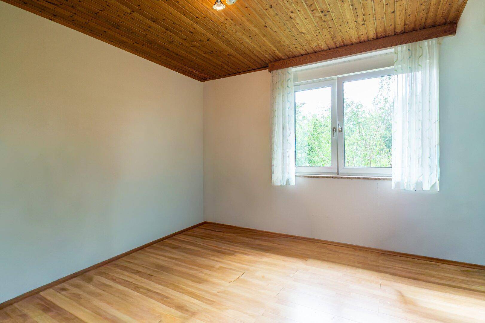 Leerer Raum mit Holzdecke und Laminatboden, bereit zur individuellen Gestaltung und Nutzung.