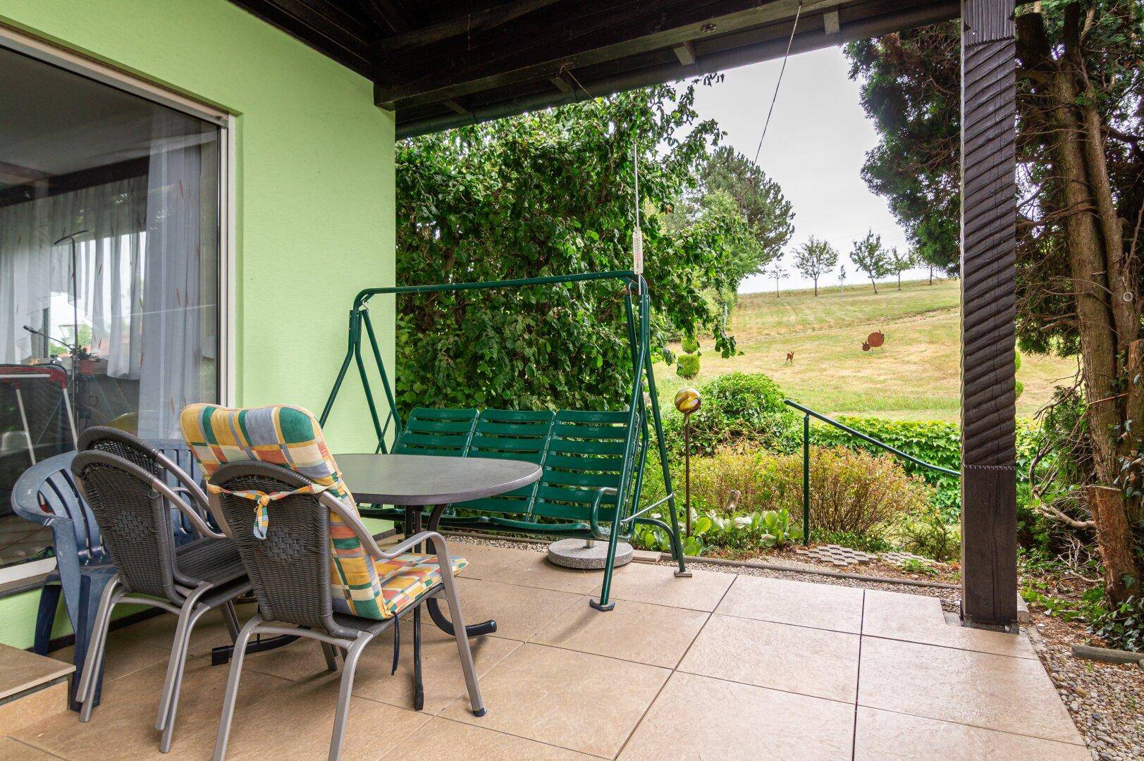 Überdachte Terrasse mit Gartenmöbeln und Blick auf den weitläufigen Garten und die Landschaft.