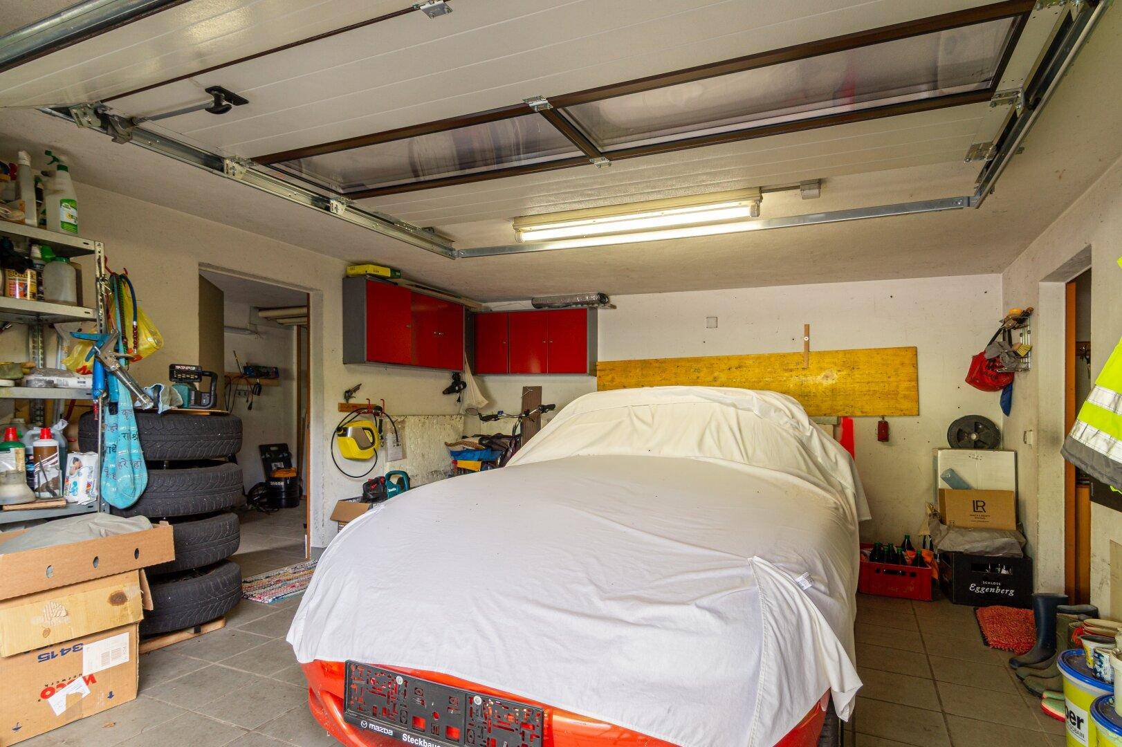 Geräumige Garage mit einem abgedeckten Auto und viel Stauraum für Werkzeuge und Reifen.