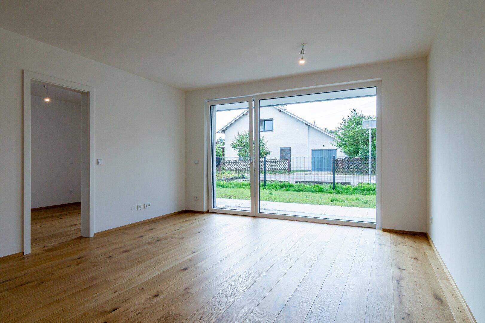 Geräumiges, unmöbliertes Wohnzimmer mit hellem Holzboden und Zugang zum Außenbereich.