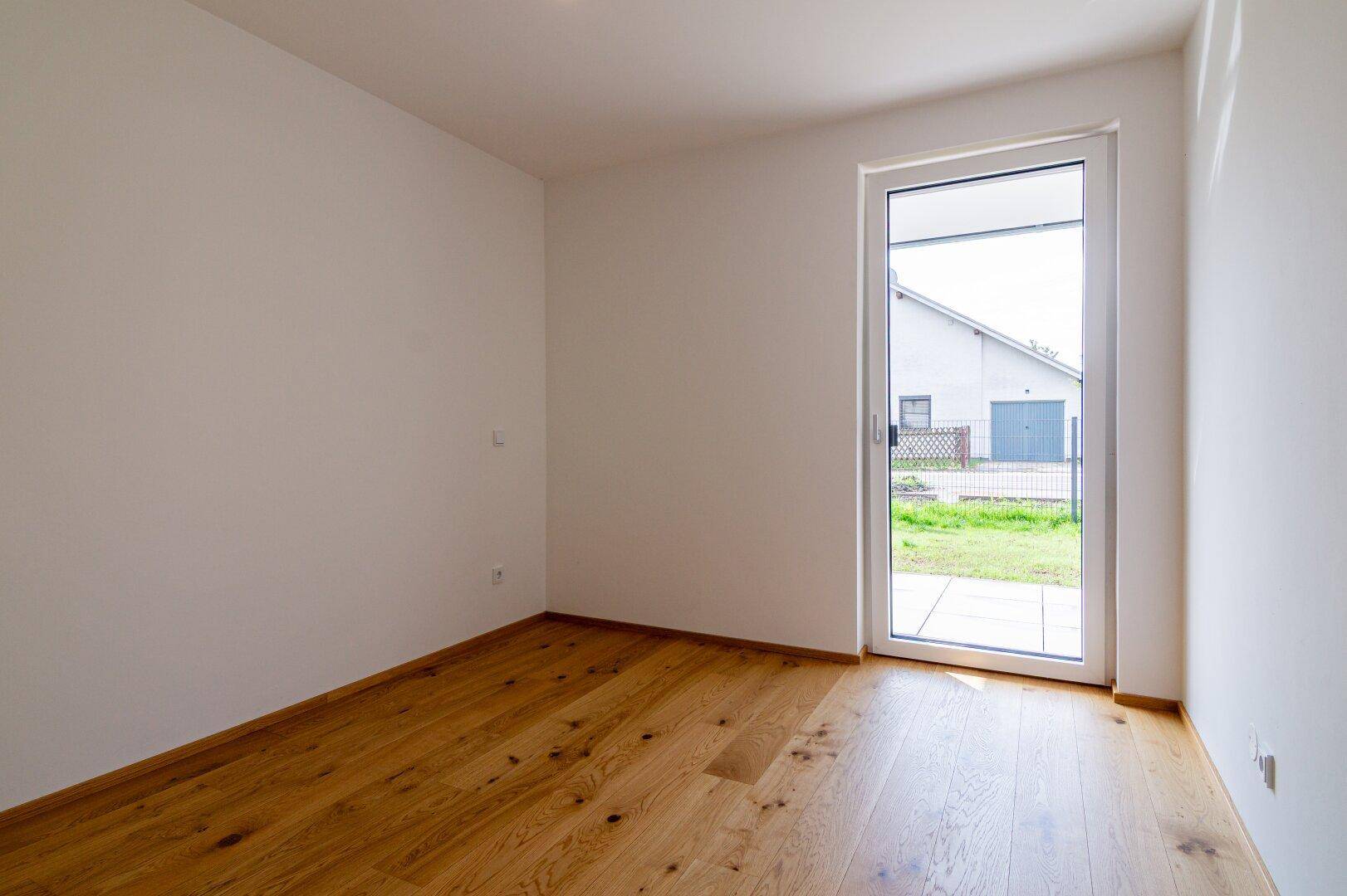 Unmöbliertes Zimmer mit Holzboden und einer Glastür, die den Zugang zum Außenbereich ermöglicht.