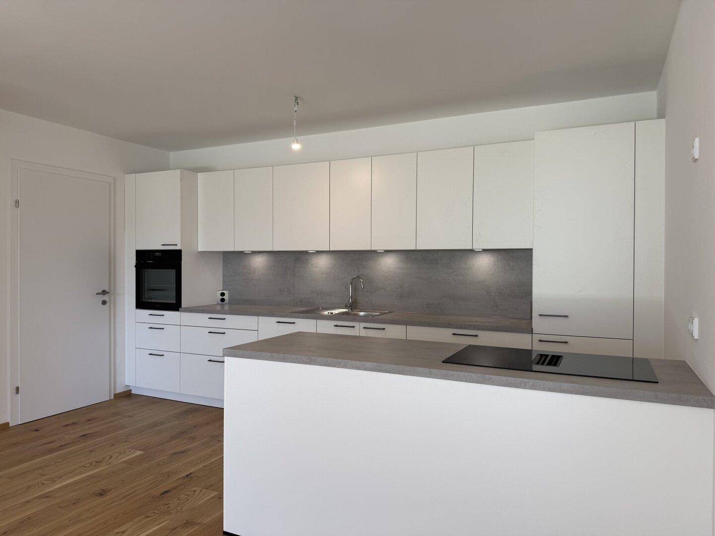 Moderne Einbauküche in Weiß mit Kücheninsel, integriertem Kochfeld und hellem Holzfußboden.