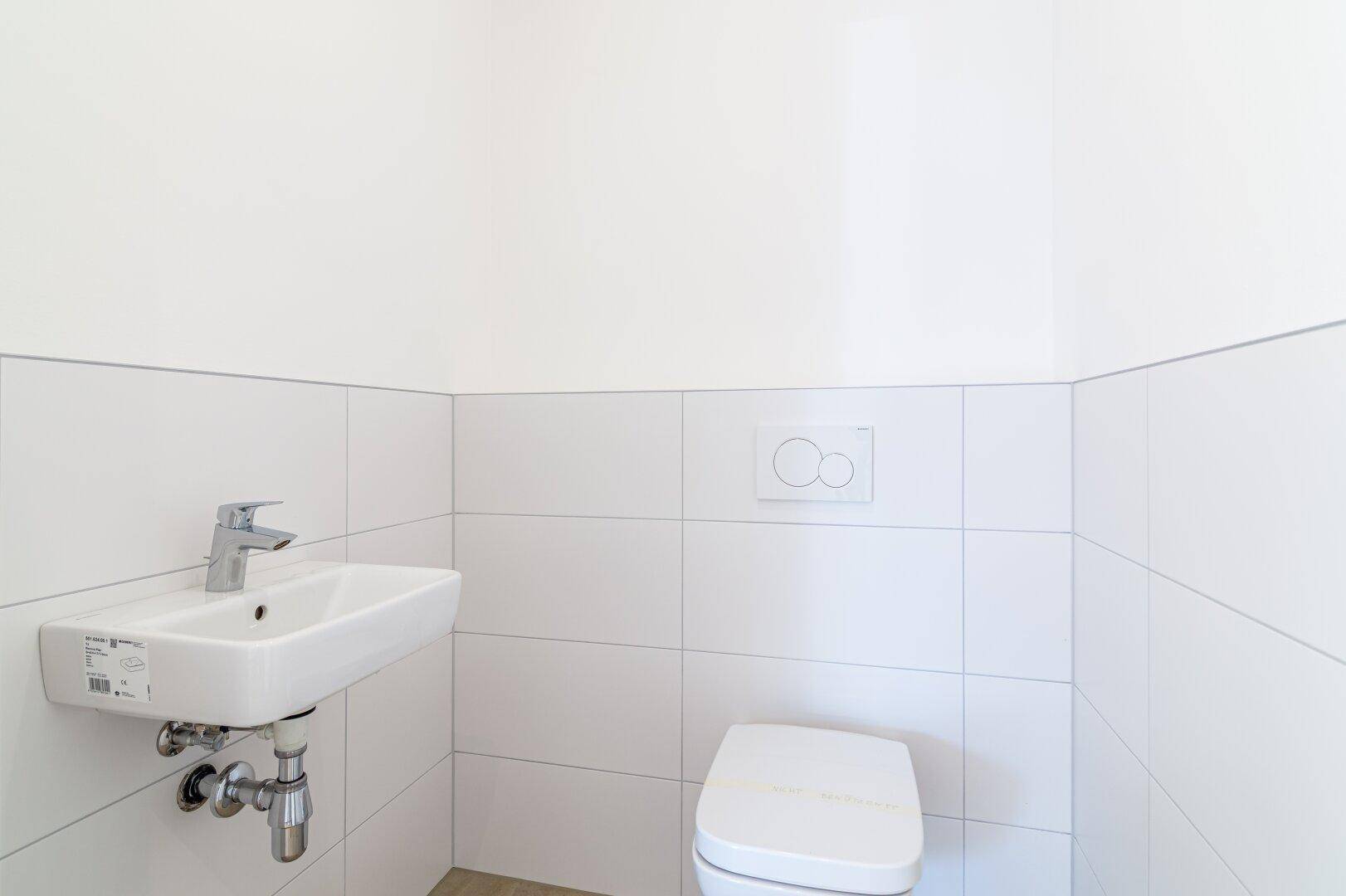 Gäste-WC mit weißen Fliesen, modernem Waschbecken und wandhängender Toilette.