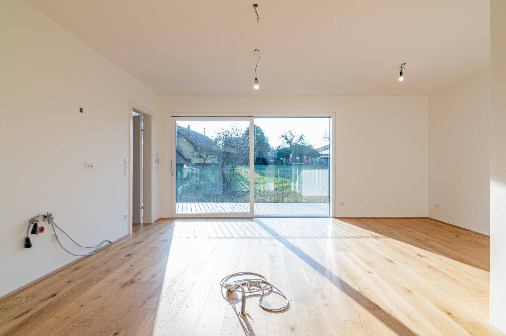 Heller Wohnbereich mit Holzboden und vorbereiteten Anschlüssen für eine offene Küche.