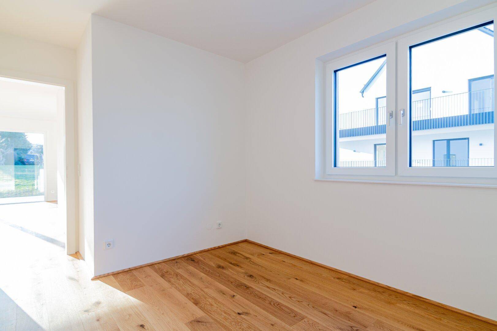 Geräumiges Schlafzimmer mit Holzboden und Blick auf moderne Architektur.