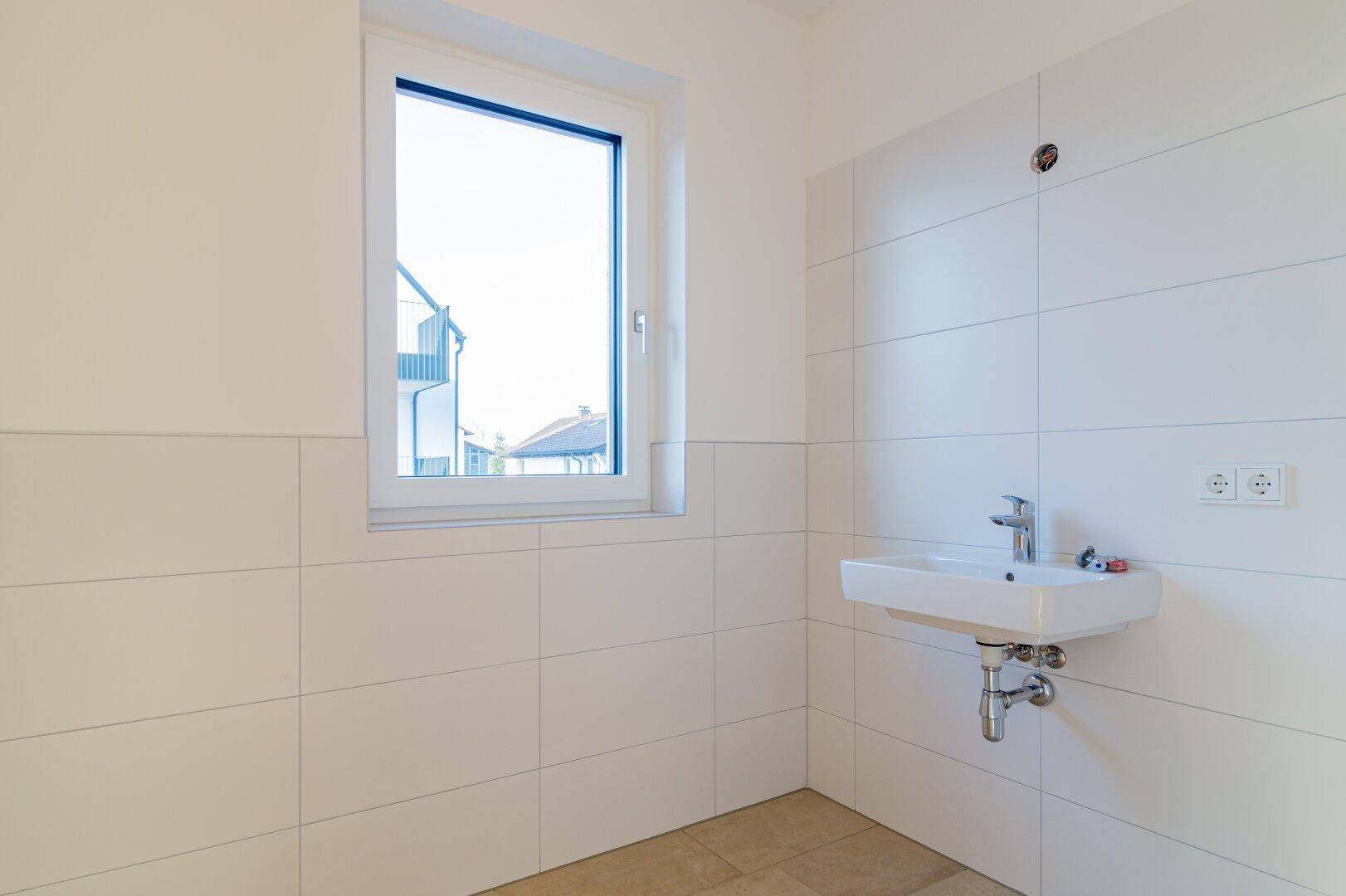 Modernes Badezimmer mit weißen Fliesen, Einzelwaschbecken und einem Fenster für Tageslicht.