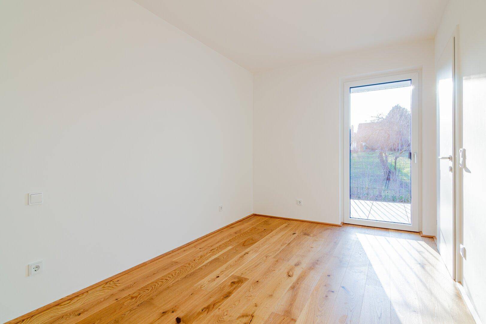 Helles Schlafzimmer mit Holzboden und direktem Zugang zu einem kleinen Balkon.