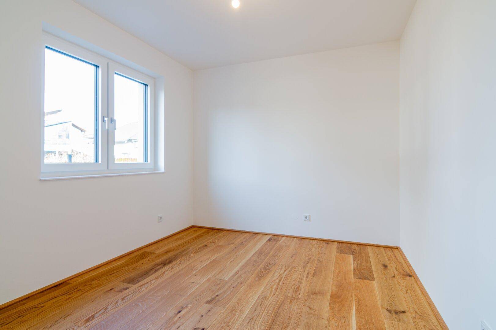 Helles Zimmer mit weiß gestrichenen Wänden und neuem Holzfußboden, ideal als Schlaf- oder Arbeitszimmer.