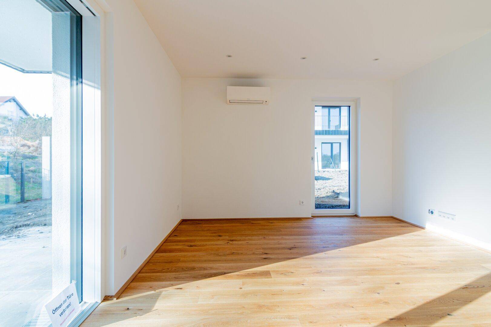 Sonniger Wohnbereich mit Holzboden, Klimaanlage und weitem Blick durch die großen Fensterfronten.