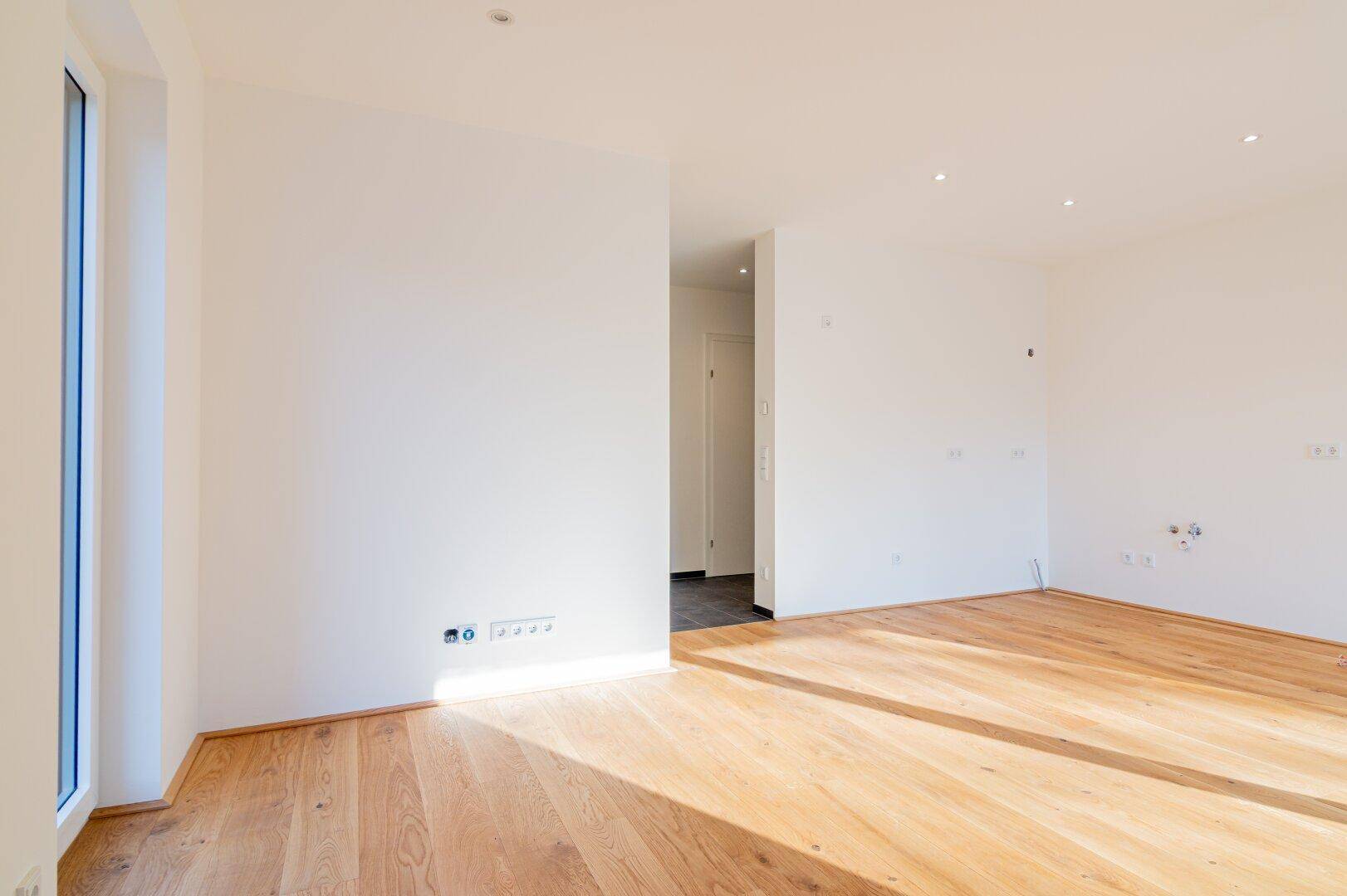 Heller Wohnraum mit Holzboden und einem schmalen Fenster, das viel Tageslicht hereinlässt.
