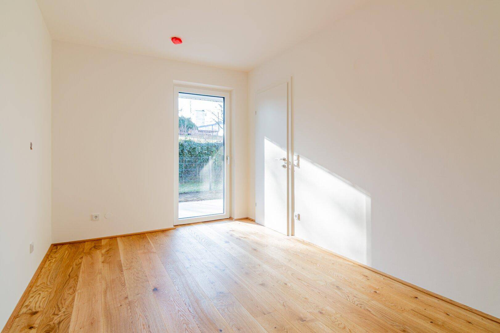 Helles Zimmer mit Holzboden und einer Glastür, die direkten Zugang zum Außenbereich ermöglicht.