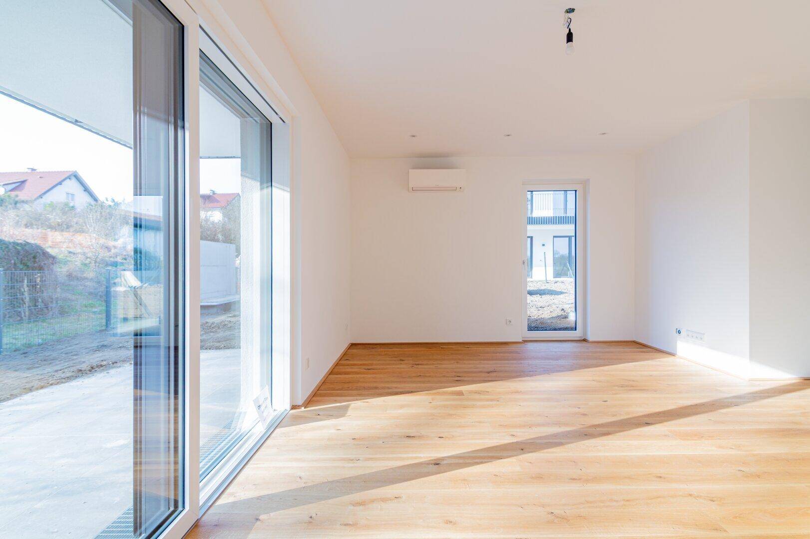 Lichtdurchfluteter Wohnbereich mit Holzboden, Klimaanlage und großen Fensterfronten zum Außenbereich.