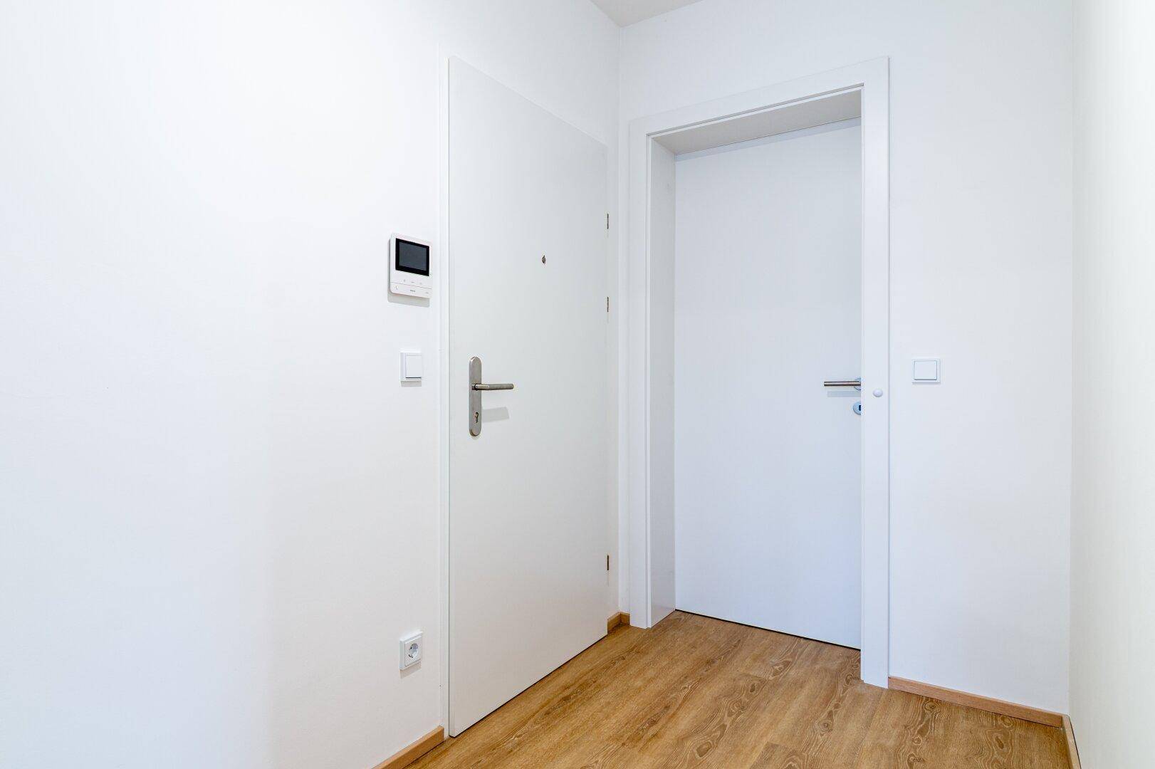 Heller Eingangsbereich mit Laminatboden und weißen Türen, die zu den Zimmern führen.