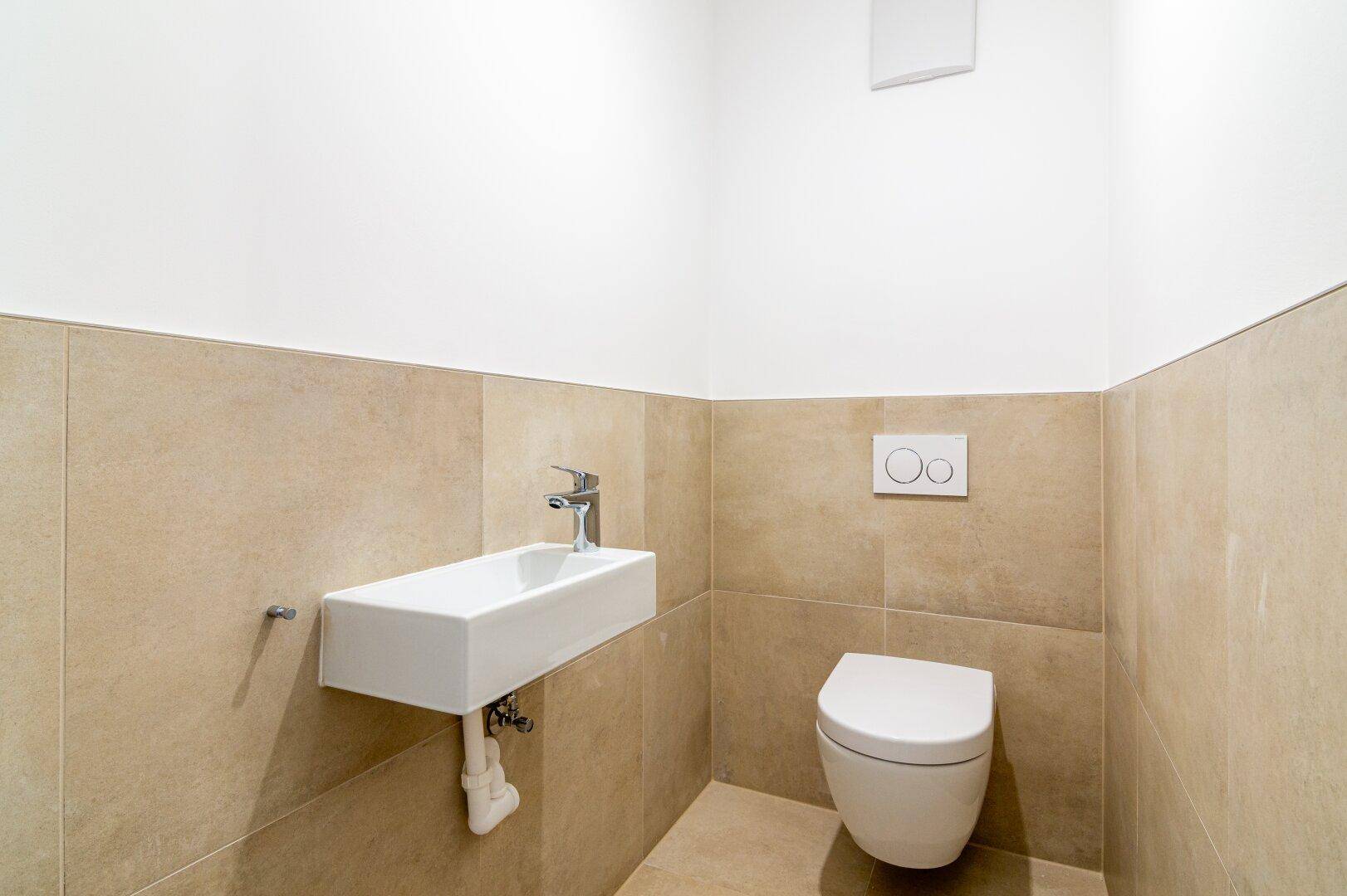 Modernes Gäste-WC mit beigefarbenen Fliesen, wandhängendem WC und kleinem Waschbecken.