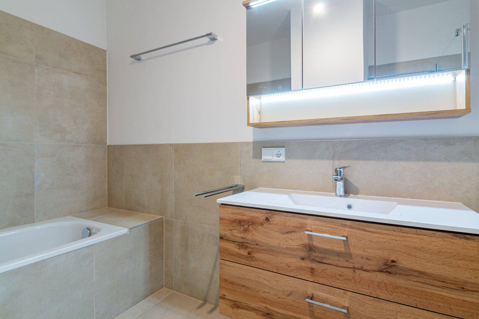 Modernes Badezimmer mit Holzwaschtisch, Spiegelschrank und beigefarbenen Wandfliesen.