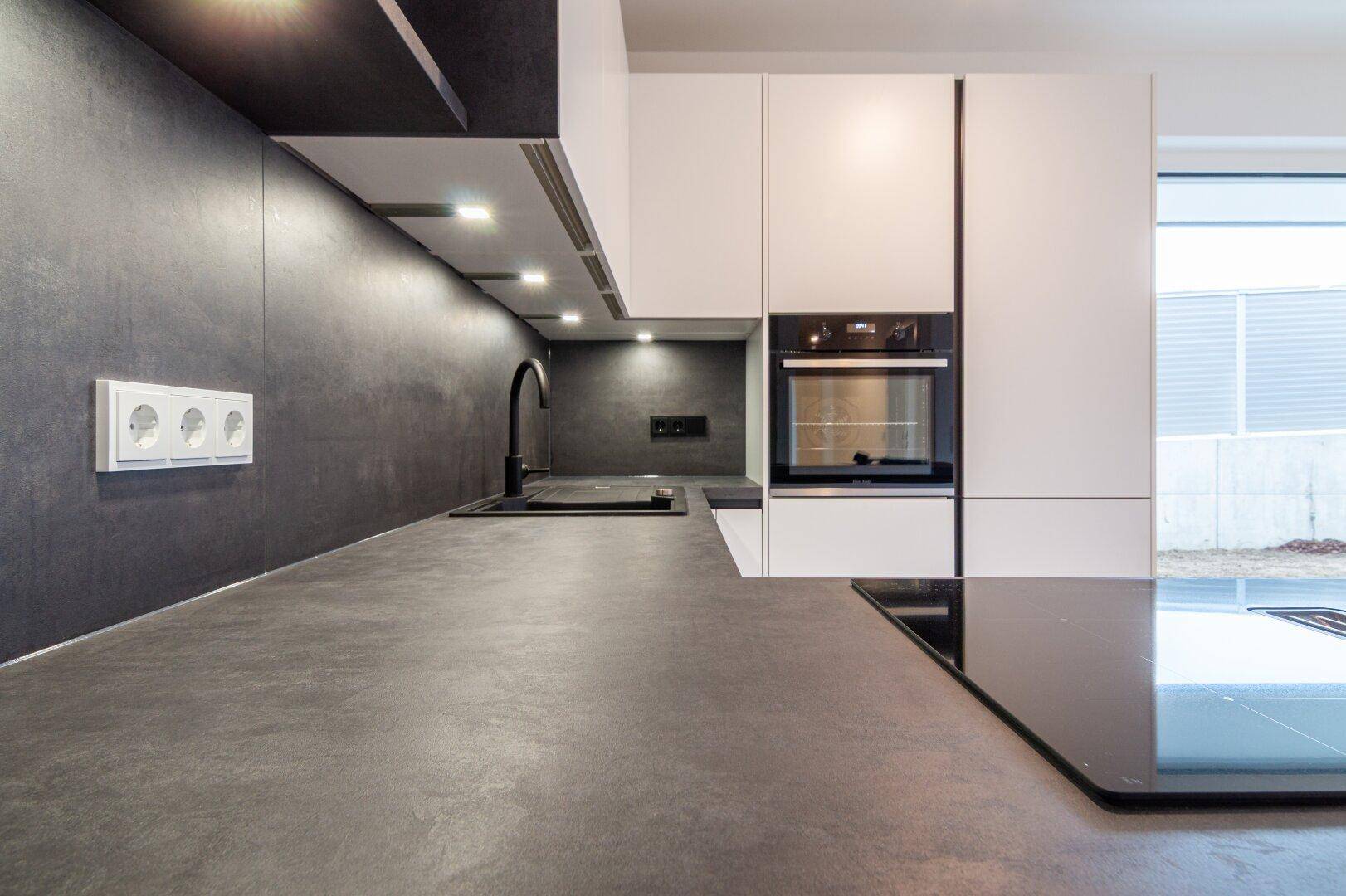 Detailansicht einer modernen Küche mit dunkler Arbeitsplatte, integriertem Kochfeld und Backofen.