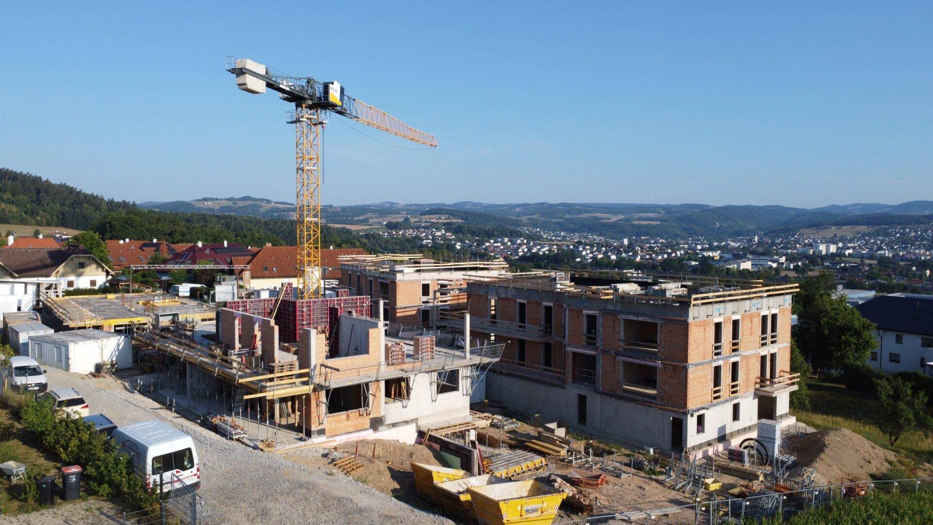 Baustelle eines neuen Wohnkomplexes mit Kran und Rohbauten unter blauem Himmel.