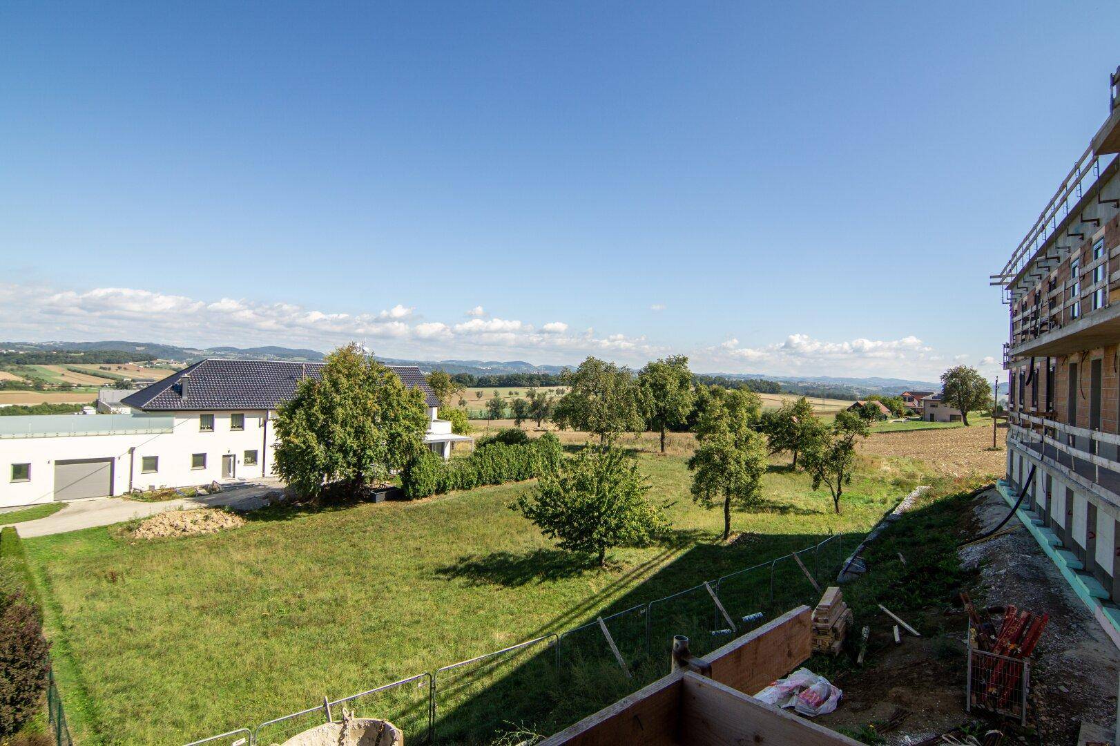 Weitläufiger Blick über die ländliche Umgebung mit Feldern, Bäumen und einem Neubauprojekt.