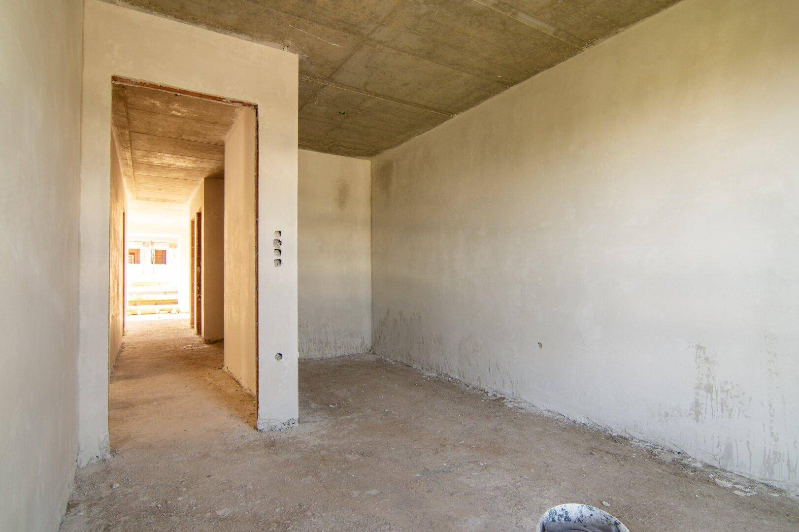 Unfertiger Raum mit Betonboden und verputzten Wänden, bereit für den Ausbau.