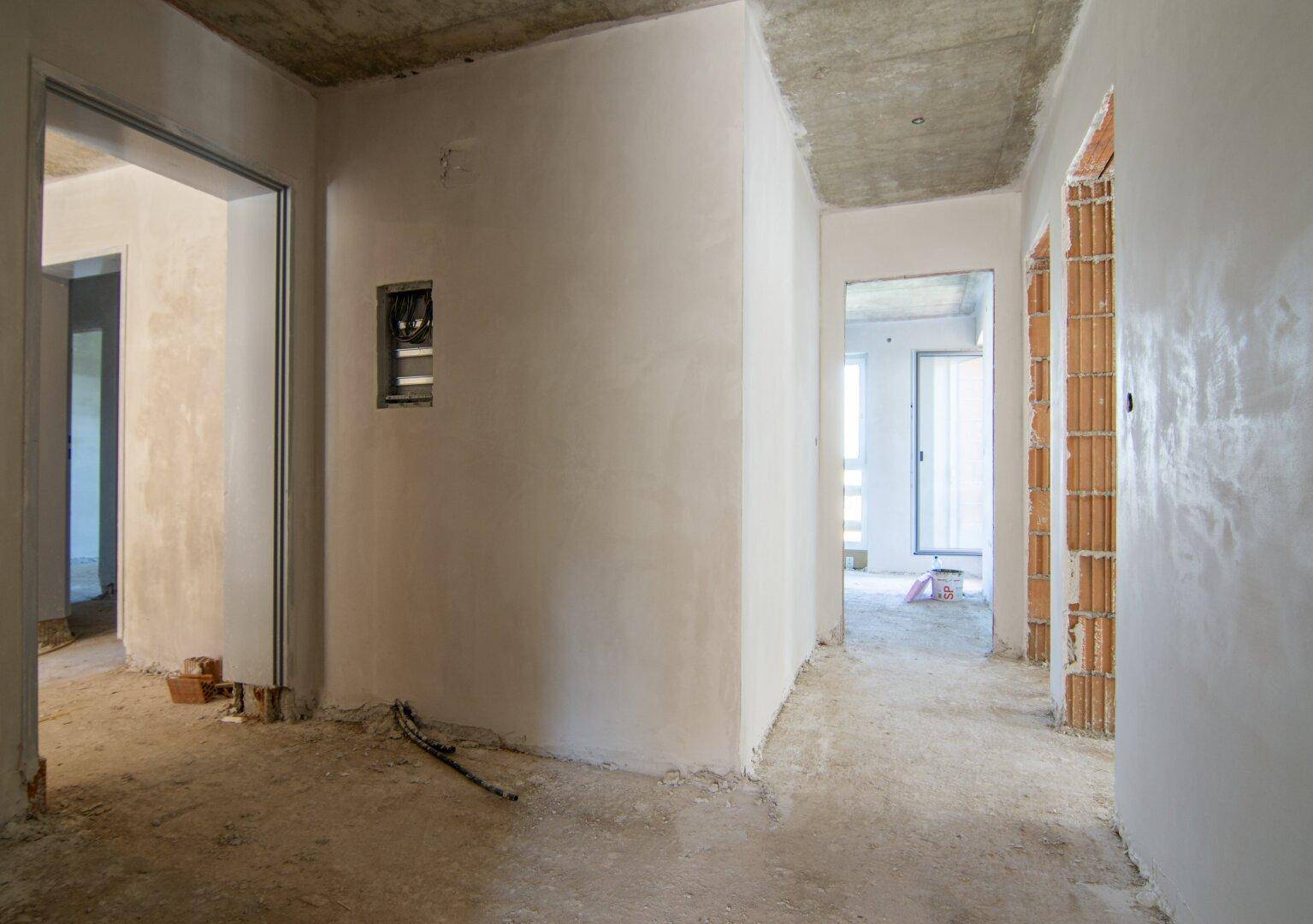 Rohbau-Innenraum mit verputzten Wänden und sichtbaren Ziegelstrukturen.
