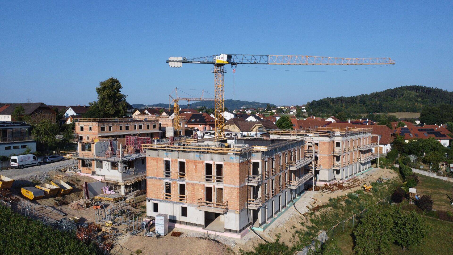 Überblick über die Baustelle mit mehreren Gebäuden im Rohbau und der umliegenden Landschaft.