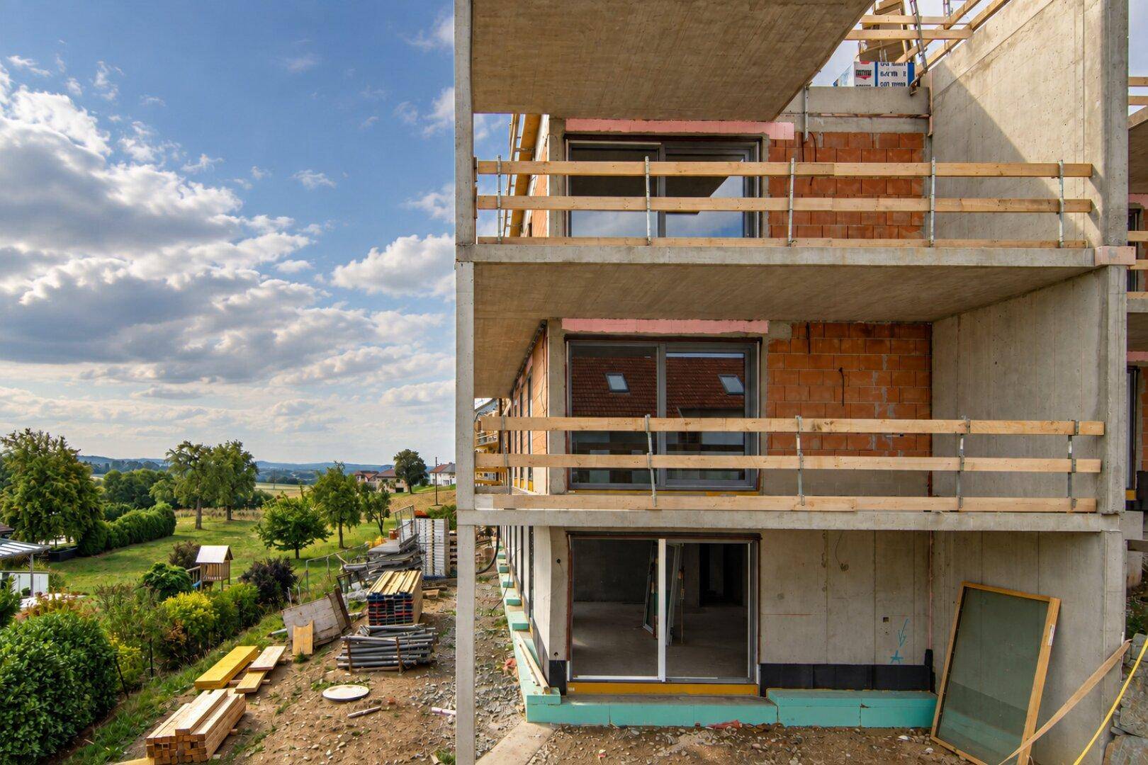 Fassade eines Neubaus im Rohbau mit mehreren Balkonen und Blick ins Grüne.