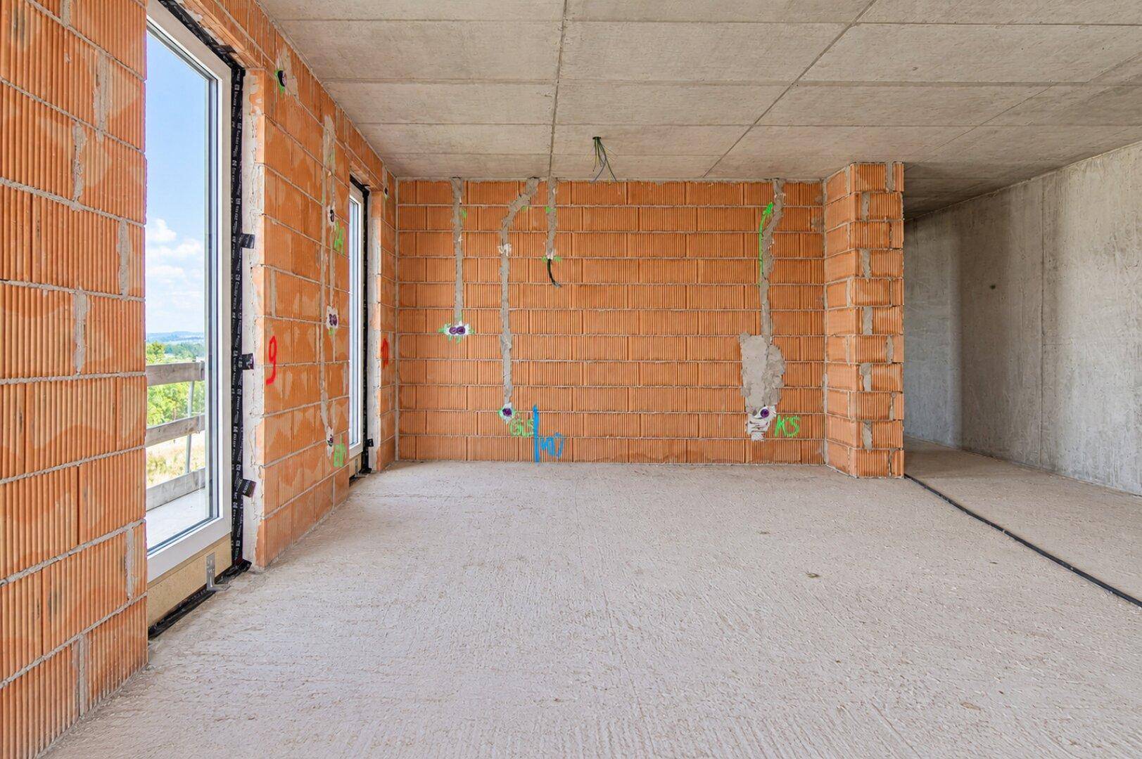 Rohbau eines Zimmers mit Ziegelwänden, Betonboden und sichtbaren Elektroinstallationen.