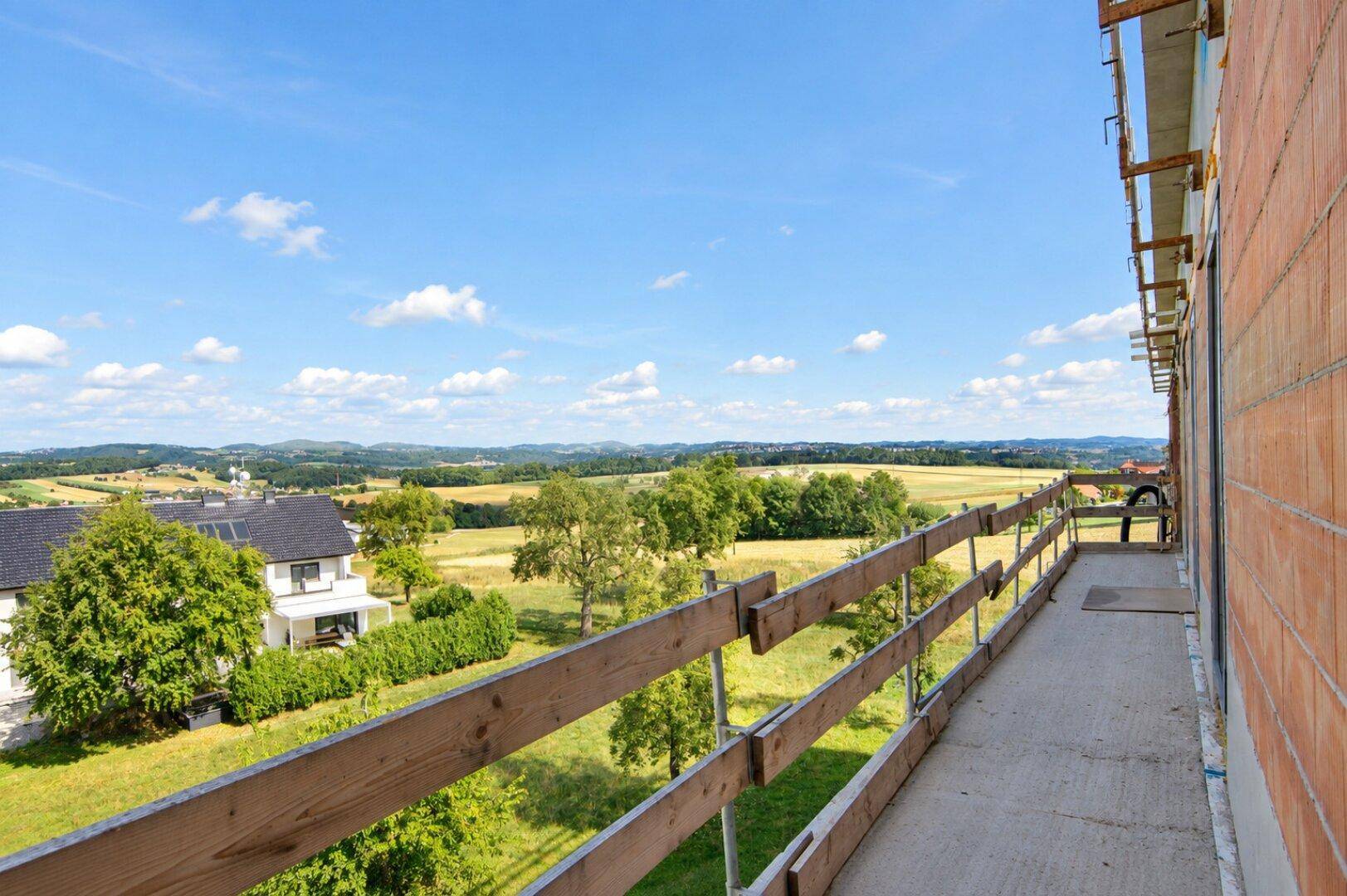 Unfertiger Balkon mit Holzgeländer und einem weiten, sonnigen Blick über die Landschaft.
