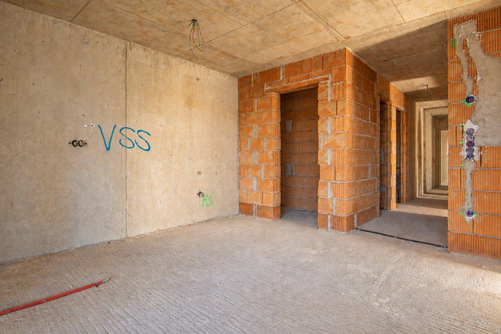 Unfertiger Innenraum im Rohbau mit Betonboden und Ziegelwänden, bereit für den weiteren Ausbau.