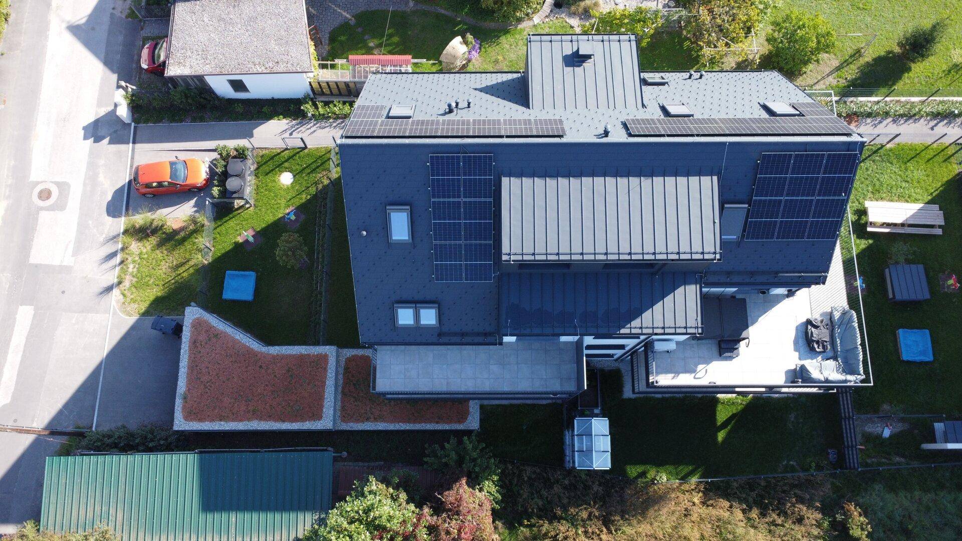 Draufsicht auf ein modernes Gebäude mit dunklem Dach, Photovoltaikanlage und angrenzendem Gartenbereich.