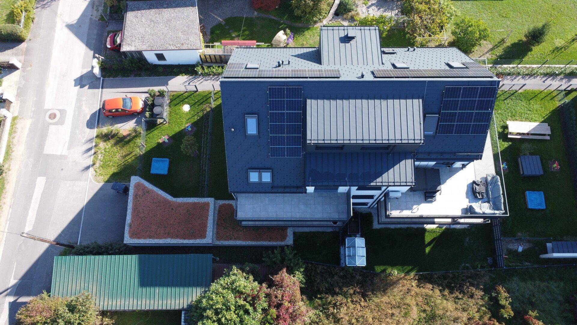 Luftaufnahme eines modernen Gebäudes mit Solaranlagen, Terrasse und angrenzendem Gartenbereich.