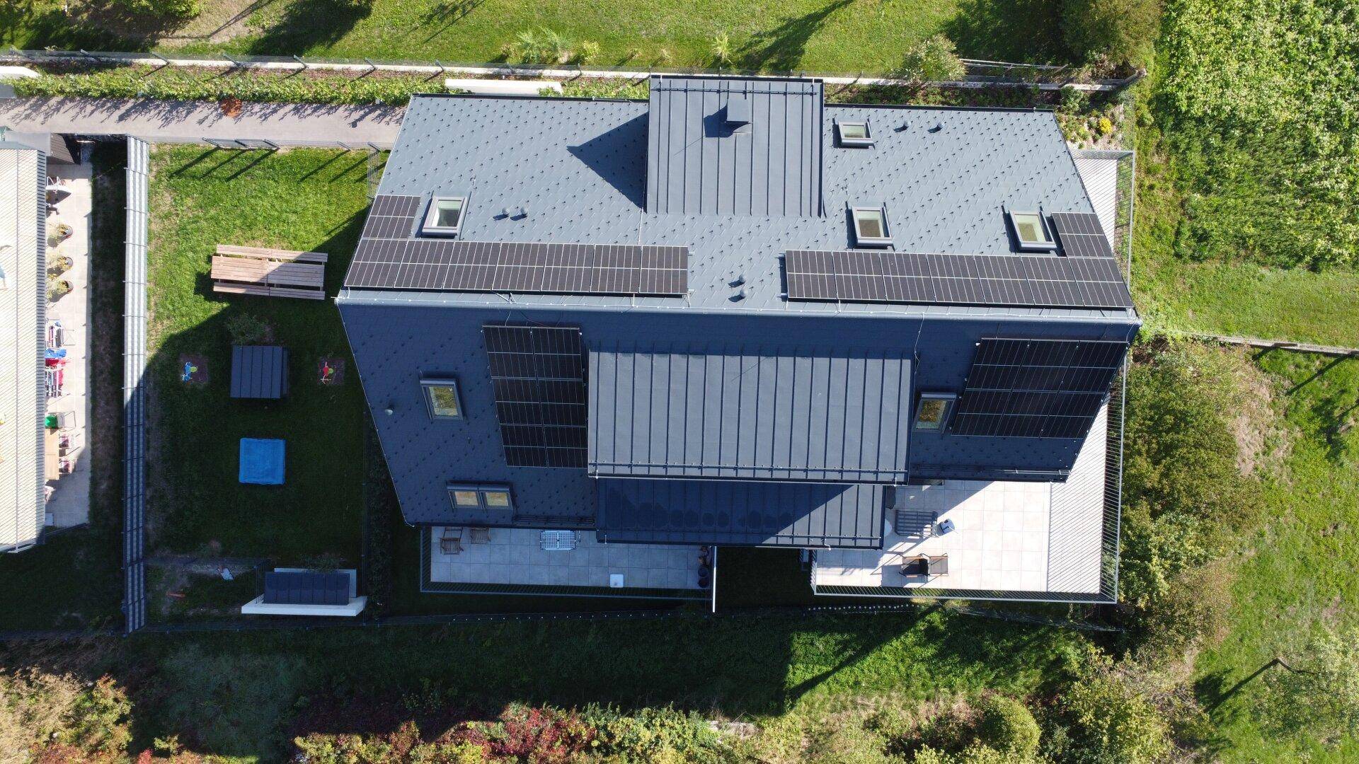 Luftaufnahme eines modernen Gebäudes mit Solaranlagen auf dem Dach und großzügigen Außenbereichen.