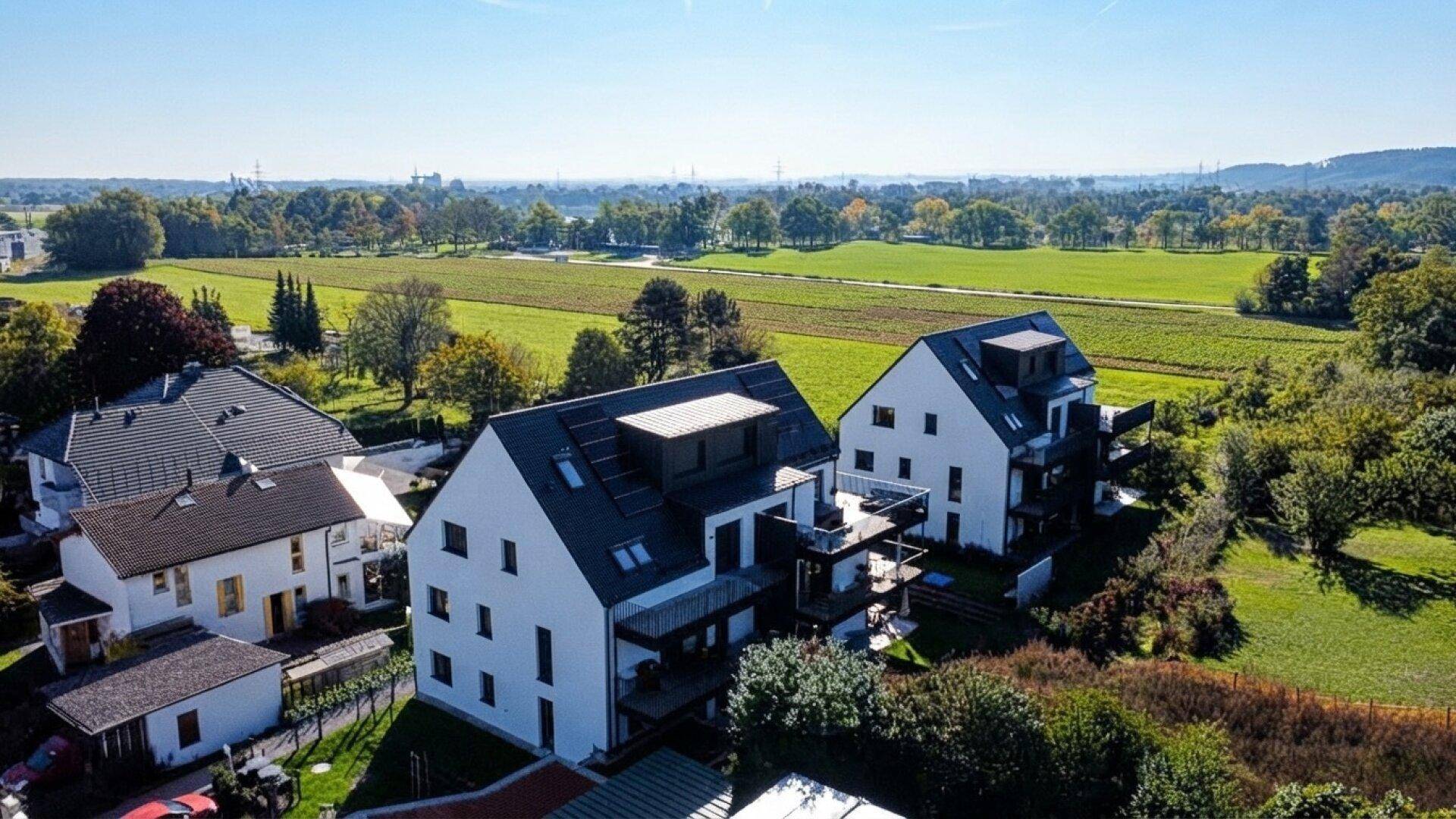 Moderne Wohngebäude mit Balkonen und Solaranlagen, umgeben von weiten Feldern und grüner Landschaft.