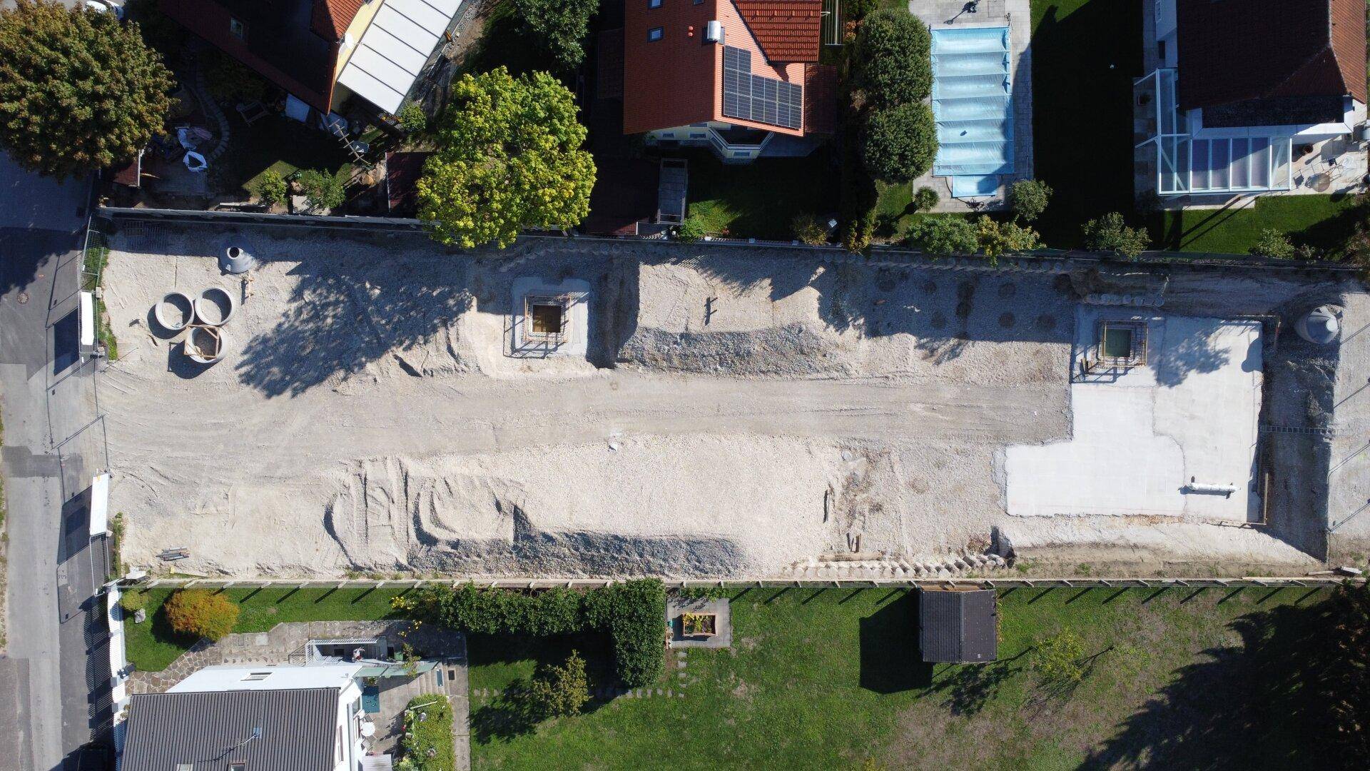 Draufsicht auf ein Baugrundstück mit vorbereitetem Fundament und angrenzenden Gärten.