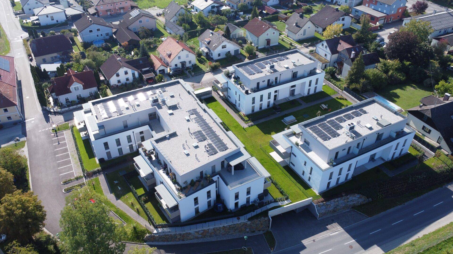 Luftaufnahme von mehreren modernen Wohngebäuden mit Solaranlagen auf den Dächern und umliegenden Grünflächen.