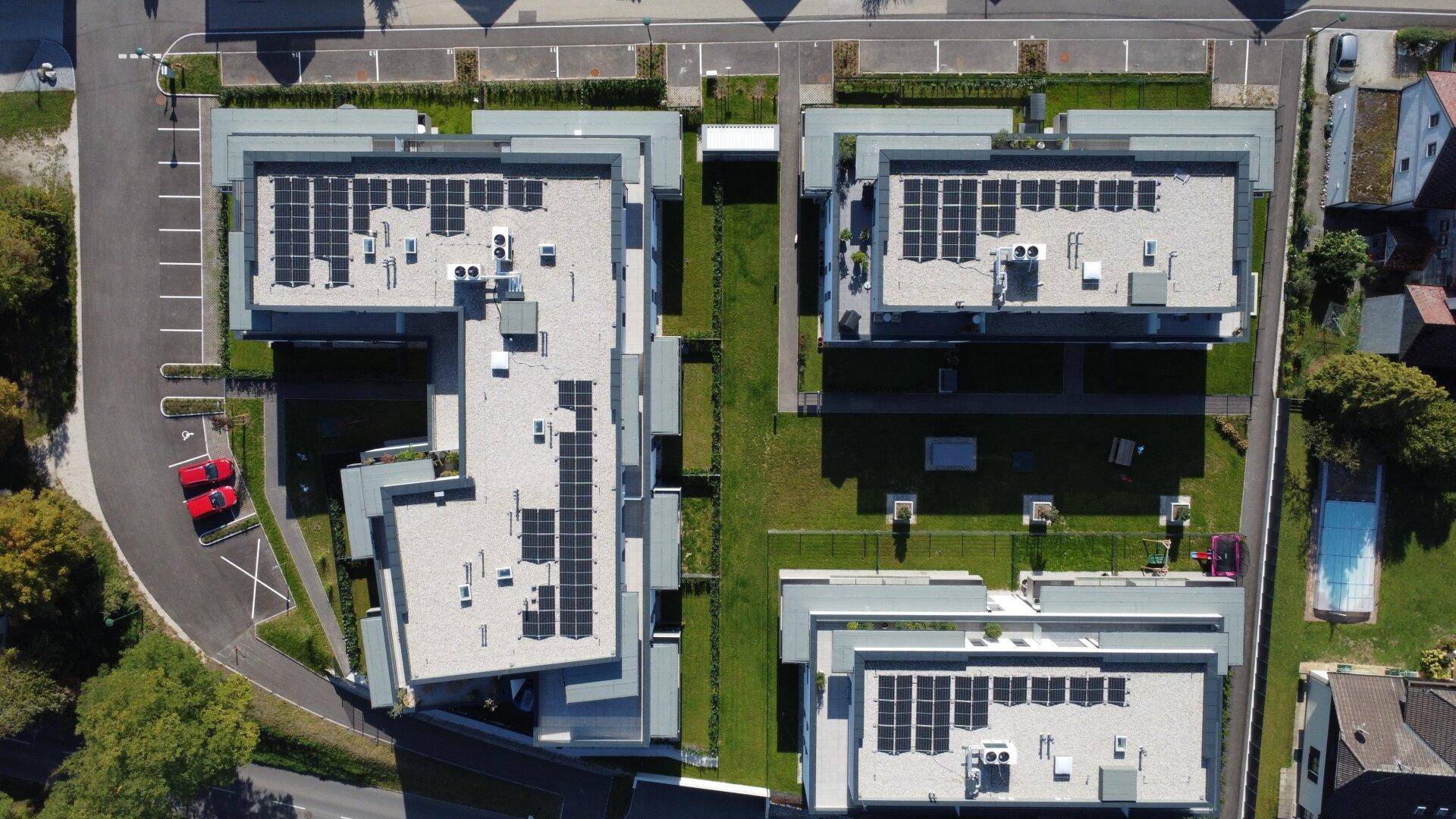 Senkrechte Luftaufnahme der Wohnanlage mit Photovoltaikanlagen auf den Flachdächern und Grünflächen.