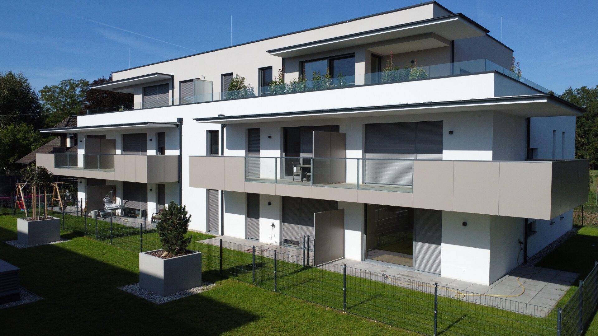 Zeitgenössisches Mehrfamilienhaus mit klaren Linien, großzügigen Balkonen und umliegender Rasenfläche.