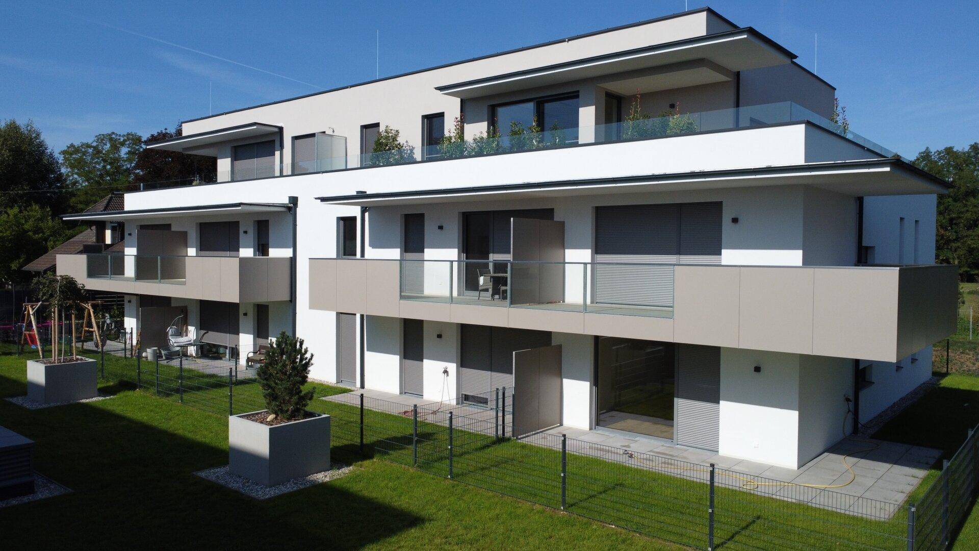 Neubau-Wohnanlage mit modernen Balkonen und Terrassen, umgeben von gepflegten Grünflächen.