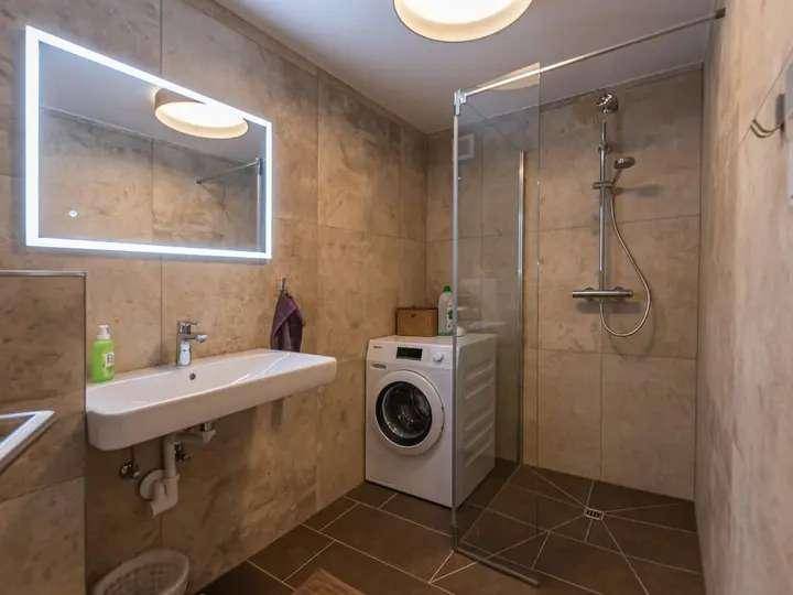Modernes Badezimmer mit begehbarer Dusche, Waschbecken und integrierter Waschmaschine.