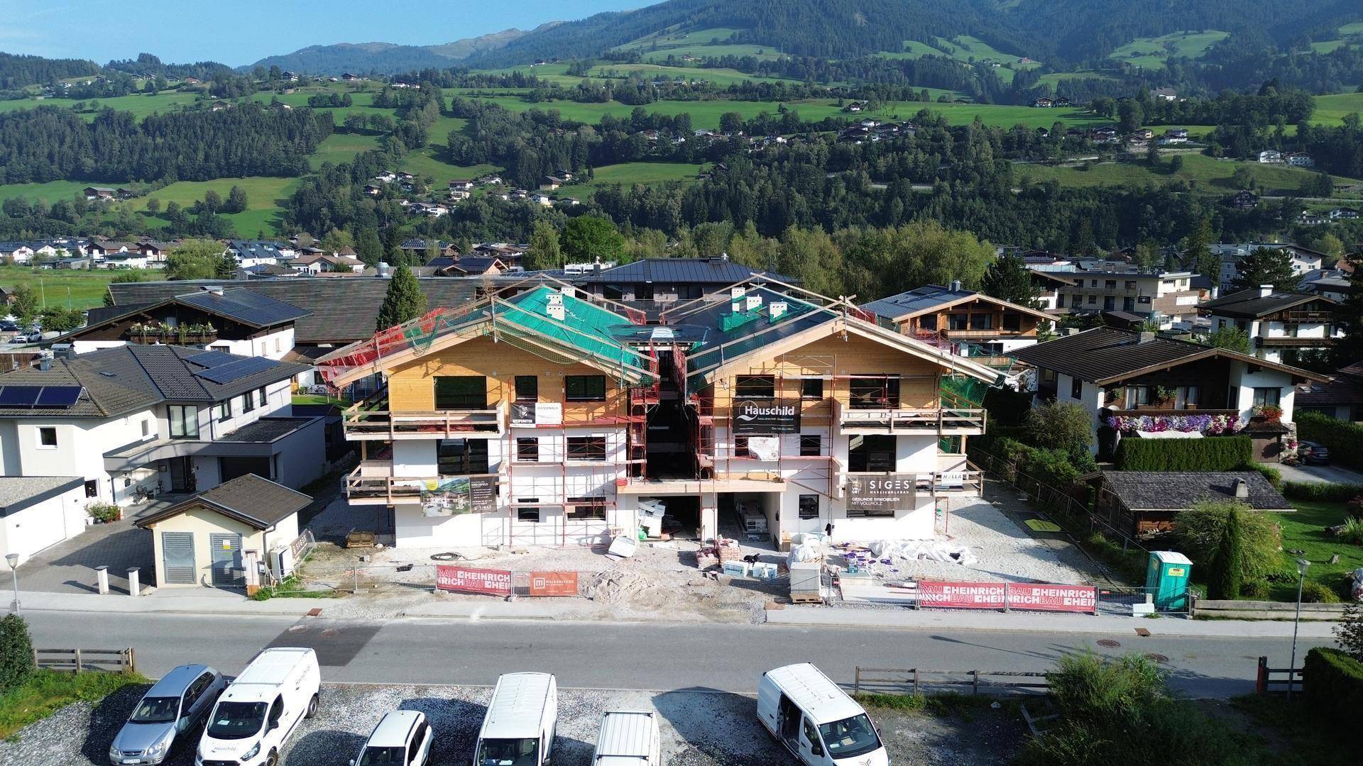 Luftaufnahme von Neubauten in Holzbauweise, eingebettet in eine grüne Berglandschaft.